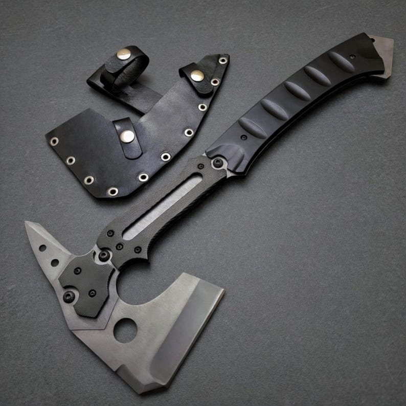 Pu&ograve; includere: Un tomahawk tattico con manico nero e lama grigia. L'ascia &egrave; dotata di un fodero in pelle con passante per cintura. Il design include una punta sul retro della testa e un foro vicino alla lama.