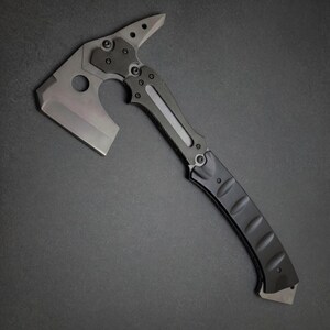 Pu&ograve; includere: Un tomahawk tattico con una lama grigia e un manico nero. La testa presenta una lama d'ascia affilata, una punta e un ritaglio circolare. L'impugnatura ha un'impugnatura strutturata per una presa sicura. Il design generale &egrave; elegante e moderno.