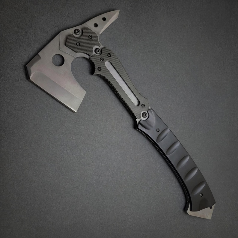 Pu&ograve; includere: Un tomahawk tattico con una lama grigia e un manico nero. La testa presenta una lama d'ascia affilata, una punta e un ritaglio circolare. L'impugnatura ha un'impugnatura strutturata per una presa sicura. Il design generale &egrave; elegante e moderno.