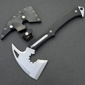 May include: A black and silver hatchet with a curved handle and a protective leather sheath. The hatchet blade has a unique design with a cutout and a sharp edge. The sheath is black with silver rivets.