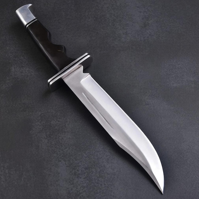 May include: A stainless steel hunting knife with a black handle and a silver bolster. The blade is curved and has a sharp edge. The knife is set against a dark background.