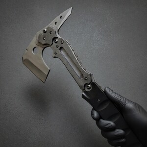 Pu&ograve; includere: Un'ascia tattica tomahawk con lama argentata e manico nero. L'ascia presenta una lama affilata, una punta e un'impugnatura strutturata per una presa sicura. Il design include un foro vicino alla lama.