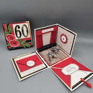 以下が含まれることがあります： 黒、赤、金色の配色が施された、手作りの多層グリーティングカード。赤いカーテンのあるステージ、小さなテーブルセッティング、数字の60が特徴です。カードは開き、複数の層を明らかにします。