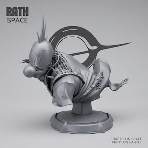 Puede incluir: Una escultura gris de un busto de payaso futurista con un casco puntiagudo, una nariz grande y una armadura detallada. La escultura está montada sobre un pedestal, con el texto "RATH SPACE" y "CRAFTED IN SPACE PRINT ON EARTH".