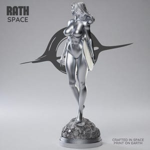 May include: A silver statue of a woman holding a surfboard, standing on a textured base. The statue has long hair and is wearing a swimsuit. The words "RATH SPACE" are at the top left. The words "CRAFTED IN SPACE PRINT ON EARTH" are at the bottom right.