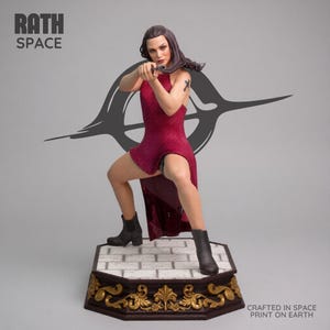 May include: A figurine of a woman in a red dress holding a gun, posed in a dynamic stance. The figure is on a decorative base with gold accents and a brick-like pattern. The text "RATH SPACE" and "CRAFTED IN SPACE PRINT ON EARTH" are visible.