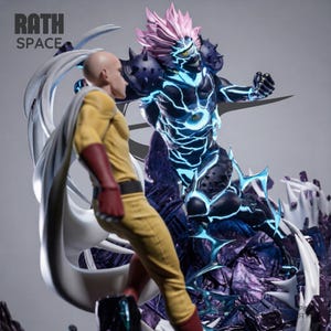 May include: A detailed statue depicting two characters from the anime series, One-Punch Man. One character is in a yellow jumpsuit with a white cape, and the other is a large, muscular figure with blue energy effects. The statue has the text "RATH SPACE".