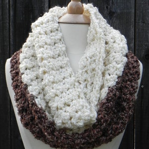 Könnte beinhalten: Ein gehäkelter Infinity-Schal mit einem weißen Mittelteil und braunen Rändern. Der Schal wird auf einer Schaufensterpuppe präsentiert.