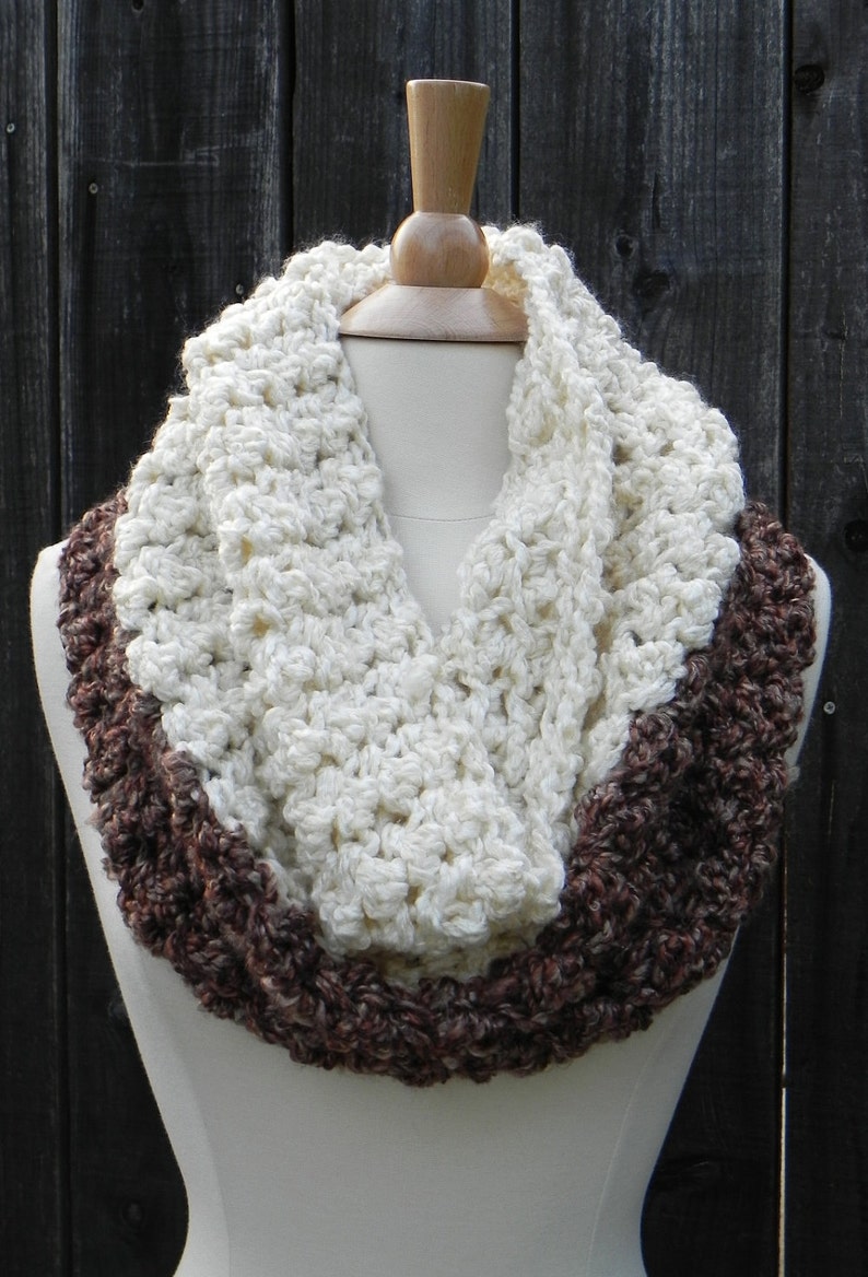Puede incluir: Una bufanda de ganchillo infinita con un centro blanco y bordes marrones. La bufanda se muestra en un maniqu&iacute;.