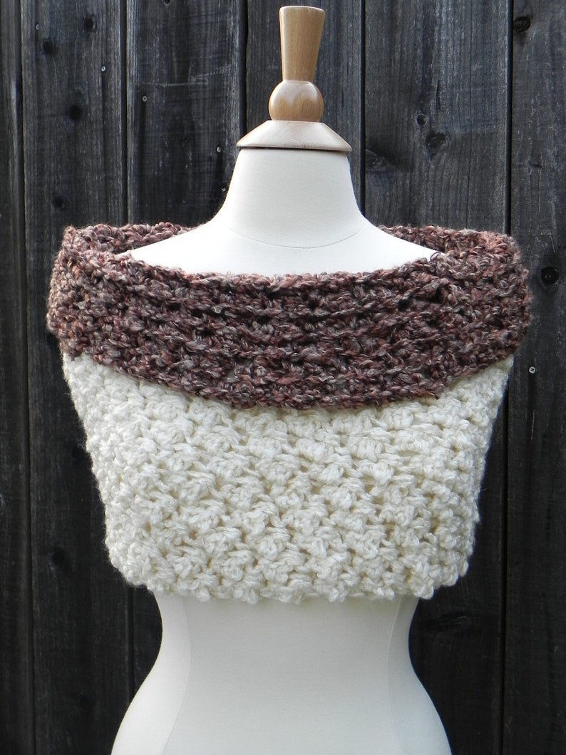 Puede incluir: Un cuello de punto de ganchillo en color marr&oacute;n y blanco. El cuello est&aacute; hecho con un punto texturizado y tiene un escote amplio y abierto.