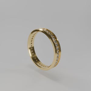 Peut inclure: Une bague en or avec une rangée continue de petits diamants clairs sertis sur les bords supérieur et inférieur. La bague a une finition polie et un design classique et élégant.