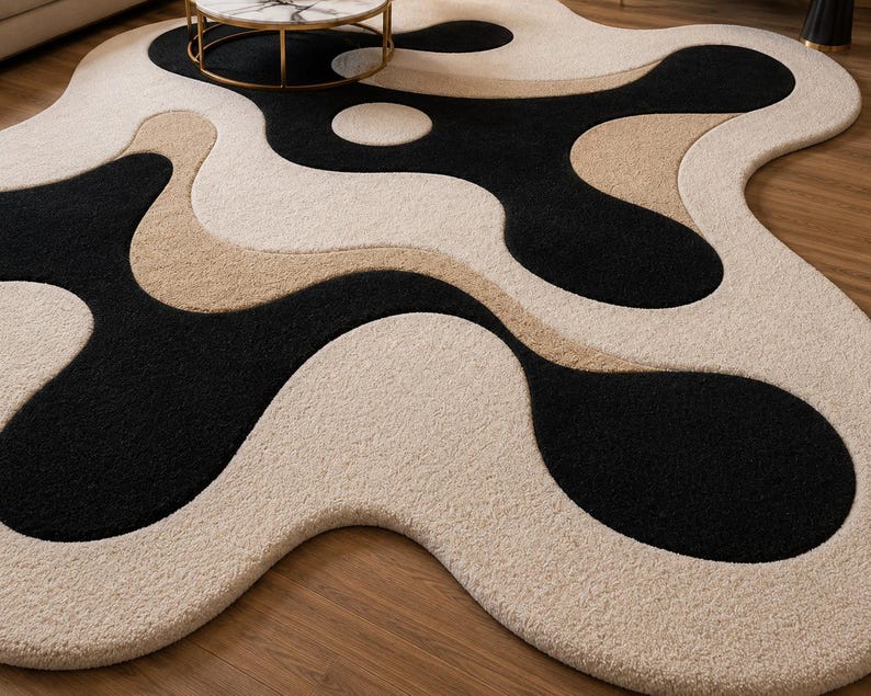 May include: A modern area rug with an abstract design. The rug features a flowing pattern of black, beige, and cream colors. The rug's unique shape and color palette create a contemporary aesthetic, suitable for living rooms or bedrooms.