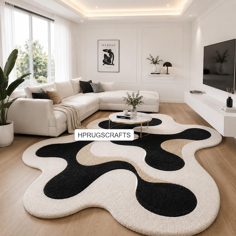 May include: A modern, abstract area rug with a unique, flowing design. The rug features a combination of black, beige, and off-white colors. The rug is placed on a hardwood floor in a living room setting. The text "HPRUGSCRAFTS" is visible.