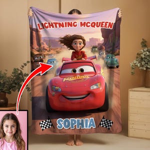 Może przedstawiać: Czerwony koc Lightning McQueen z kresk&oacute;wkowym wizerunkiem postaci z filmu Auta. Koc ma imię "Sophia" i wz&oacute;r w szachownicę. Koc jest trzymany przez osobę.