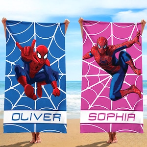 May include: Two rectangular beach towels featuring Spider-Man graphics. One towel is blue with a white spiderweb pattern and the name OLIVER. The other towel is pink with a white spiderweb pattern and the name SOPHIA. Both display the character in action.