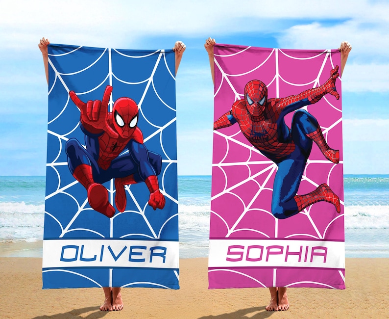 May include: Two rectangular beach towels featuring Spider-Man graphics. One towel is blue with a white spiderweb pattern and the name OLIVER. The other towel is pink with a white spiderweb pattern and the name SOPHIA. Both display the character in action.