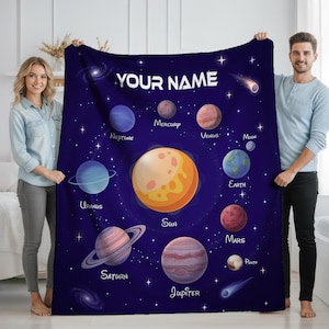 May include: A dark blue blanket with a colourful illustration of the solar system, including the sun and planets. The blanket has the text "YOUR NAME" at the top. Planets are labelled with their names. A great gift for astronomy lovers.