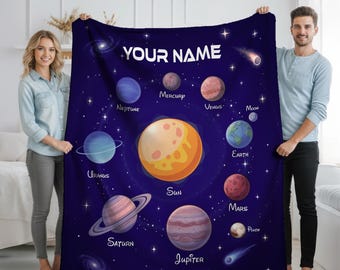 May include: A dark blue blanket featuring a colorful illustration of the solar system, including the sun and planets. The blanket has the text "YOUR NAME" at the top. Planets are labeled with their names. A great gift for astronomy lovers.