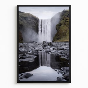 Puede incluir: Impresión enmarcada de un paisaje con una poderosa cascada que cae en un estanque de agua. La escena incluye rocas oscuras y colinas verdes bajo un cielo nublado. El reflejo de la cascada es visible.