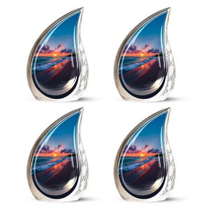 May include: Four teardrop-shaped pendants with a sunset beach scene reflected inside. Each pendant has a silver-colored frame and a decorative pattern on the side. The sunset features orange, red, and blue hues.