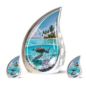 May include: A large teardrop-shaped urn and two smaller matching teardrop-shaped keepsakes, all featuring a silver metallic frame with an engraved floral pattern and a vibrant underwater scene of a sea turtle swimming in clear blue ocean water.