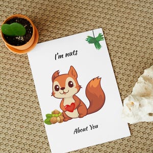 Könnte beinhalten: Eine weiße Grußkarte mit einem Cartoon-Eichhörnchen, das ein rotes Herz hält, mit dem Text "I'm nuts About You". Das Eichhörnchen ist braun und orange, mit einem flauschigen Schwanz. Haselnüsse und grüne Blätter sind unten.