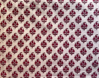 Può includere: Tessuto bianco con un motivo ripetuto di motivi floreali bordeaux. Ogni elemento floreale ha un gruppo di piccoli petali rotondi e uno stelo. Il tessuto sembra essere cotone o un materiale simile.
