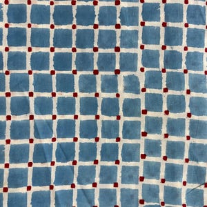 May include: A textile featuring a grid pattern of blue squares, white lines, and red dots. The blue squares have a textured look, and the design is simple and geometric. The fabric is suitable for various craft projects.