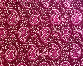 May include: A close-up of a fabric with a repeating paisley pattern. The pattern features large, teardrop-shaped motifs in shades of magenta and white against a deep burgundy background. The design is detailed and intricate, with floral elements.