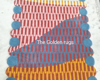 May include: A rectangular rug with a colorful geometric pattern. The rug features sections of orange, red, and blue vertical lines, with a section of orange and white oval shapes. The edges are scalloped with blue circles. The text "The Golden rugs" is visible.