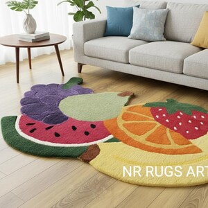 Puede incluir: Una colorida alfombra con forma de fruta que representa una rodaja de sandía, uvas, una pera, una rodaja de naranja, una fresa y un plátano. La alfombra está colocada sobre un suelo de madera. El texto "NR RUGS ART" es visible.