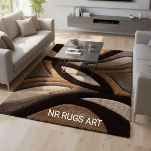 Op de afbeelding: Een modern vloerkleed met een golvend patroon in bruin, beige en grijstinten. Het kleed ligt in een woonkamer met een bank, salontafel en televisie. De tekst "NR RUGS ART" is zichtbaar op het kleed.