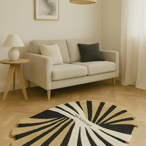 May include: A modern area rug with a fan-like design, featuring alternating black, beige, and white stripes. The rug is placed on a wooden floor in a living room setting, with a beige sofa and a round side table. The text "NR RUGS ART" is visible on the rug.