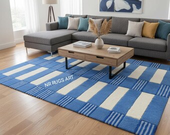 May include: A blue and white patterned area rug with a rectangular design. The rug features alternating stripes of light blue and off-white, with a border of darker blue stripes. The text "NR RUGS ART" is visible on the rug.