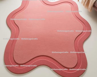 May include: A layered, wavy-edged rug in shades of pink and red. The rug features a three-dimensional design with a lighter pink center, a medium pink middle layer, and a darker red outer edge. The rug is designed for home decor.