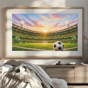 Könnte beinhalten: Ein gerahmter Wandkunstdruck, der ein Fußballstadion bei Sonnenuntergang mit einem Fußball im Vordergrund auf dem Rasen zeigt. Das Stadion ist voller Zuschauer und verfügt über helle Flutlichter vor einem farbenfrohen Himmel mit Wolken.