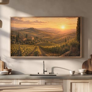 Könnte beinhalten: Ein rechteckiges gerahmtes Wandbild, das einen Sonnenuntergang über einer Weinbergslandschaft mit sanften Hügeln, Zypressen und einem Steingebäude zeigt. Das Kunstwerk hängt an einer beigen Wand über einer Küchenzeile mit hellen Holzschränken.