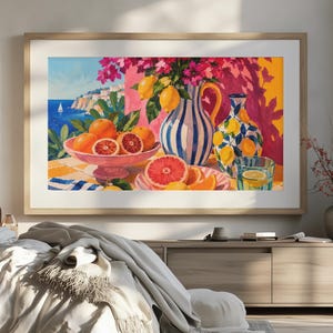 Könnte beinhalten: Ein gerahmtes Landschaftsgemälde, das eine Küstenszene mit einer Schale voller Orangen und Grapefruits, einem blau-weiß gestreiften Krug mit Zitronen und rosa Blumen sowie einem Glas Wasser auf einer gelb karierten Tischdecke zeigt.