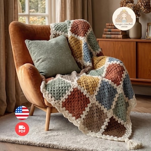 May include: A crochet blanket featuring a square pattern in shades of rust, mustard yellow, sage green, and blue, joined by cream-colored yarn. The blanket is draped over a burnt orange armchair, which also holds a solid sage green square throw pillow.
