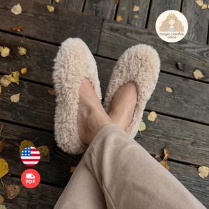 Op de afbeelding: Een paar beige, pluizige pluche slippers met een zachte, getextureerde buitenkant. De slippers hebben een rond teenontwerp en een instapmodel. Een cirkelvormig logo in de rechterbovenhoek toont de tekst magic crochet verse.