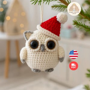 May include: A crocheted owl ornament with large black eyes and a red Santa hat. The owl is cream-colored with gray accents on the ears, beak, and feet. The ornament is hanging from a green branch.