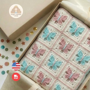 Puede incluir: Una manta de ganchillo hecha a mano con un diseño de mariposas, presentada en una caja de regalo. La manta tiene un fondo blanco con mariposas rosas y azules. La caja es beige y contiene el texto "magic crochet verse".