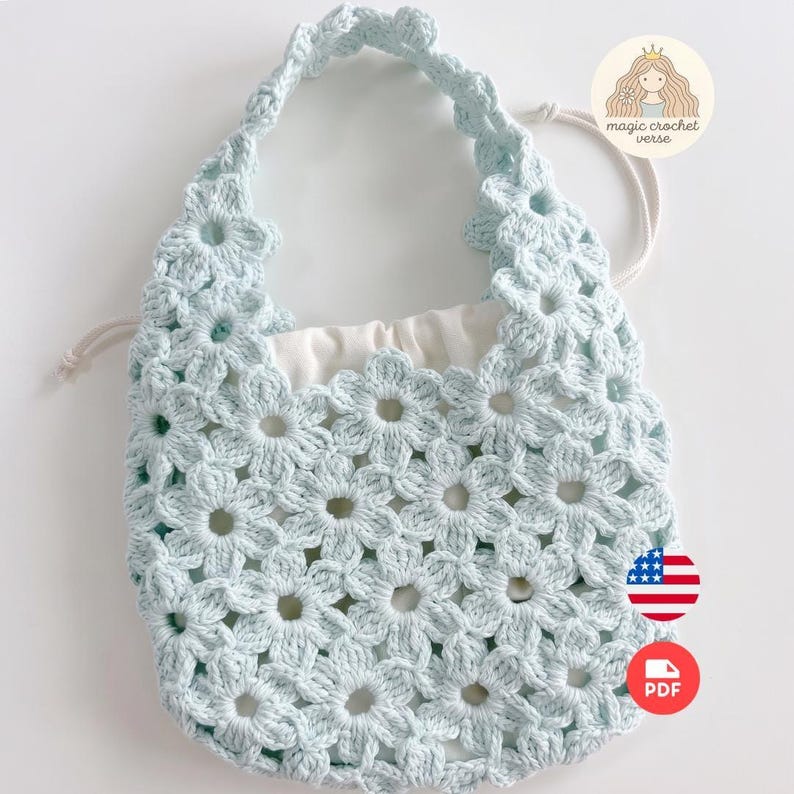 Puede incluir: Un bolso de ganchillo azul claro con un patr&oacute;n de motivos florales repetidos en todo el cuerpo y el asa. El bolso incluye un forro interior de tela blanca con cord&oacute;n y un logotipo circular en la esquina superior derecha que dice magic crochet verse.