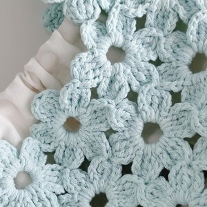 Puede incluir: Un bolso de ganchillo azul claro con un patr&oacute;n de motivos florales repetitivos. El bolso est&aacute; construido con flores de hilo interconectadas e incluye un forro de tela blanca visible a trav&eacute;s del dise&ntilde;o calado, junto con un cord&oacute;n blanco.