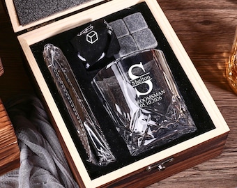 Puede incluir: Una caja de regalo de madera que contiene un vaso de cristal transparente grabado con la letra S, el nombre Shelton y el texto GROOMSMAN 05.10.2026. El set incluye una bolsa de terciopelo negro, cuatro piedras de whisky grises y pinzas metálicas.