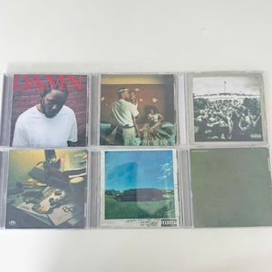 May include: A collection of six CD albums in clear plastic cases. The album covers feature various images, including a portrait of a man, a couple, and a crowd of people. The album covers are in various colors.