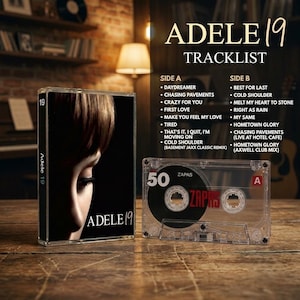May include: A clear plastic cassette case featuring the Adele 19 album cover with a close-up of a face, alongside a transparent cassette tape labeled Side A with the number 50 and the word ZAPAS printed in red on the black reel.