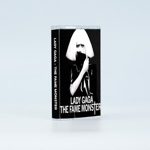 May include: A cassette tape case featuring the album cover for Lady Gaga - The Fame Monster. The black and white artwork displays a person with a blonde bob hairstyle, holding a black object near their face. The text reads Lady Gaga - The Fame Monster.