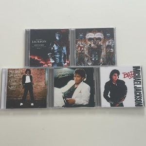 Puede incluir: Una colección de cinco álbumes en CD de Michael Jackson. Las portadas de los álbumes presentan imágenes de Michael Jackson en varias poses y atuendos. Los títulos incluyen "History", "Off the Wall", "Thriller" y "Bad". Los CD están en estuches de plástico transparente.