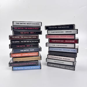May include: Two vertical stacks of music cassette tapes. The left stack features albums by The Smiths, including Meat Is Murder and The Queen Is Dead. The right stack contains Fleetwood Mac albums, such as Mirage, Rumours, and Tusk, with clear plastic cases.